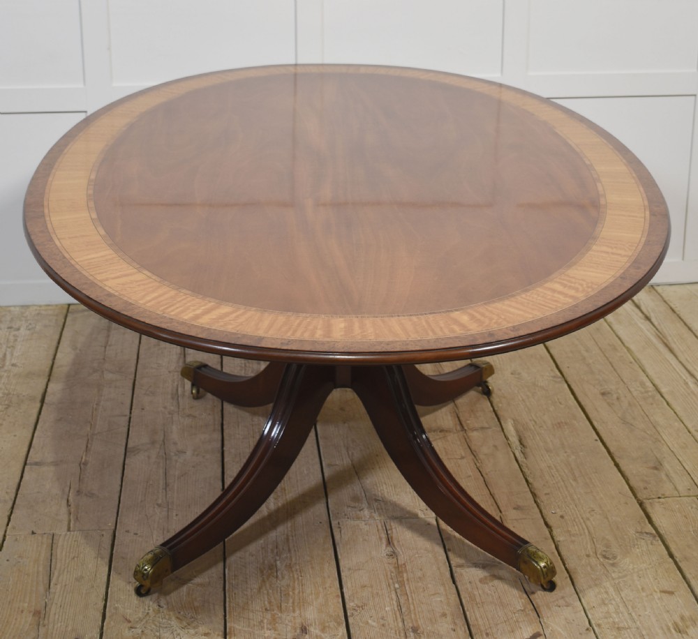 An oval mahogany dining table featuring a crossbanded satinwood border and a central pedestal with four reeded splayed legs ending in brass cap castors. View III