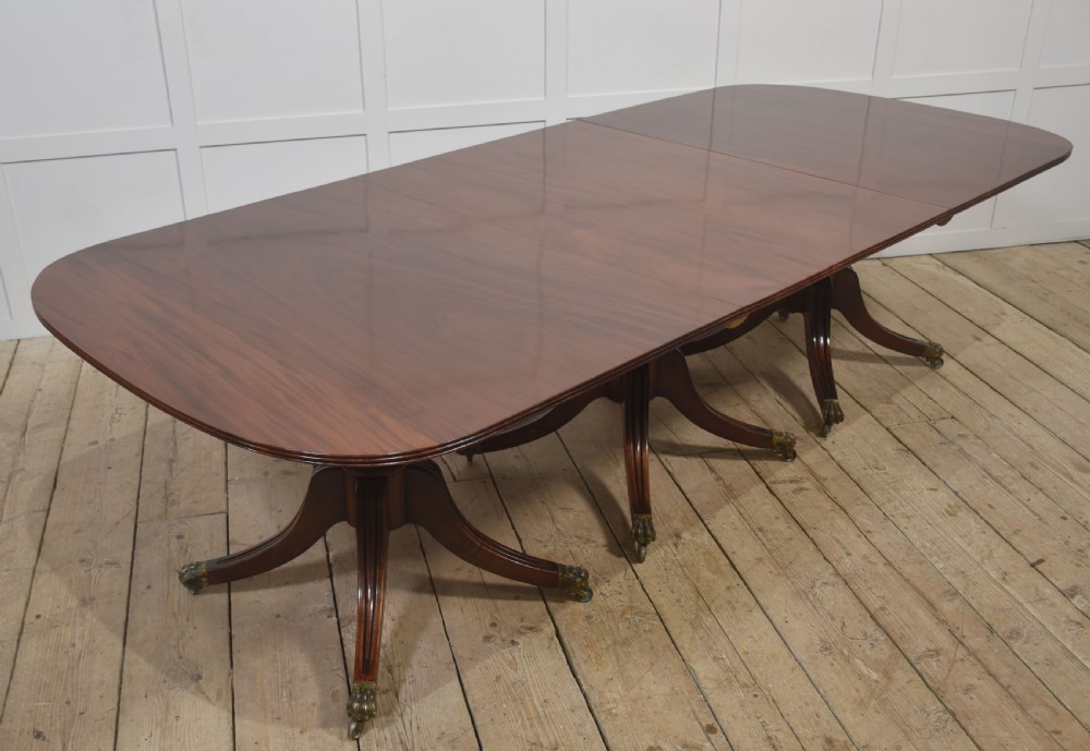 A long polished mahogany triple pedestal dining table featuring rounded corners, reeded splayed legs, and brass claw feet.