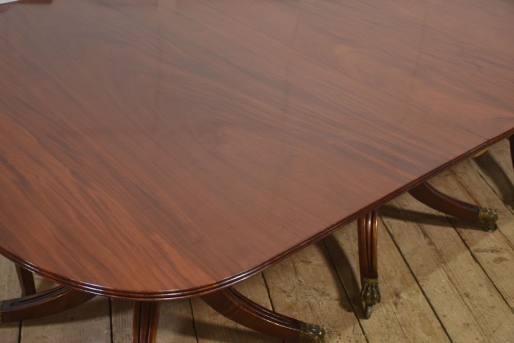 A long polished mahogany triple pedestal dining table featuring rounded corners, reeded splayed legs, and brass claw feet. View IX