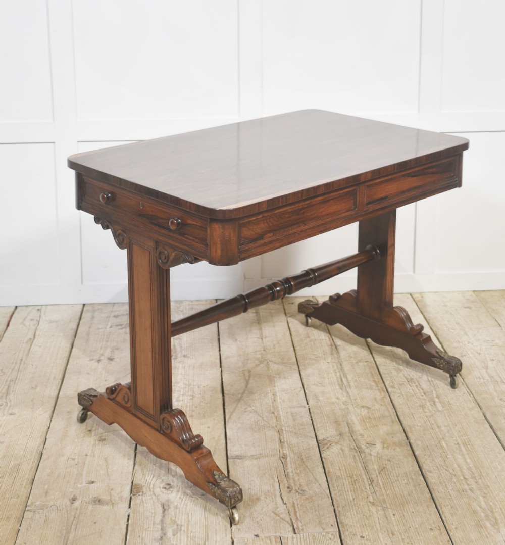 An antique Regency rosewood side table with turned stretcher and brass castors set against a white panelled wall. View II
