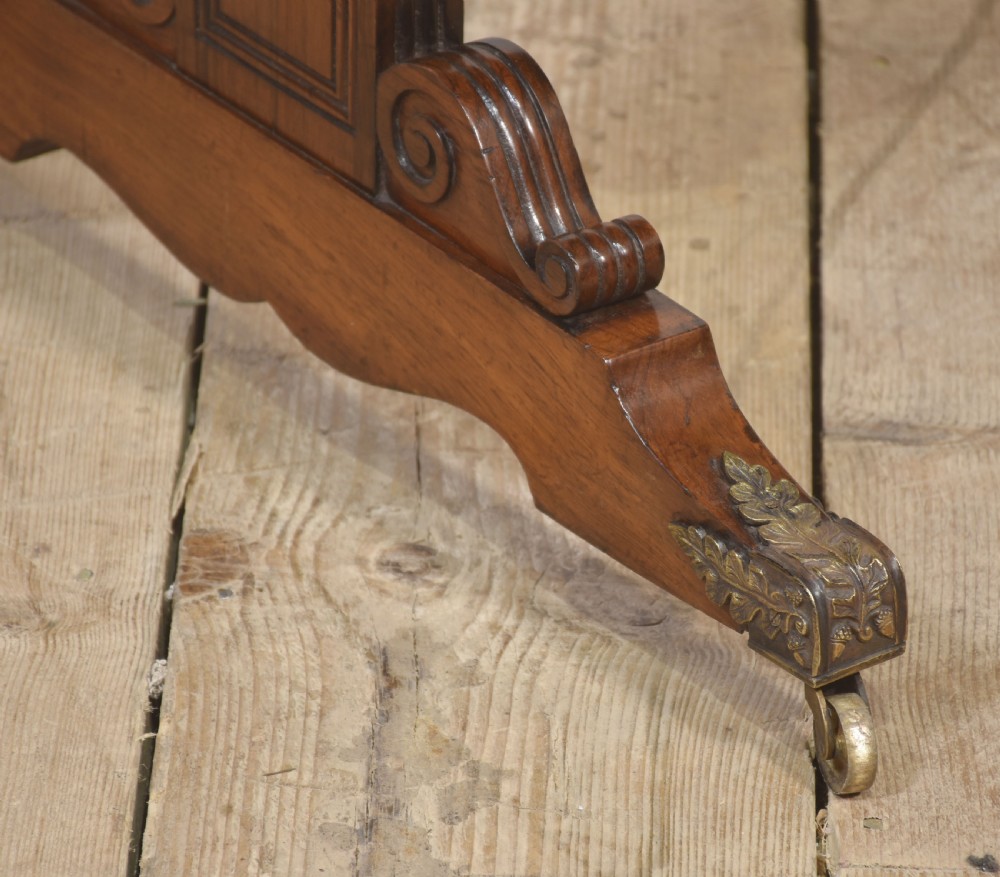 An antique Regency rosewood side table with turned stretcher and brass castors set against a white panelled wall. View III