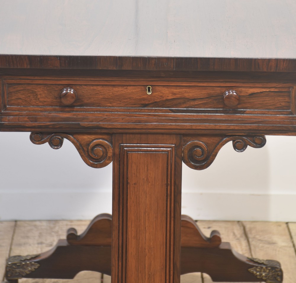 An antique Regency rosewood side table with turned stretcher and brass castors set against a white panelled wall. View VI