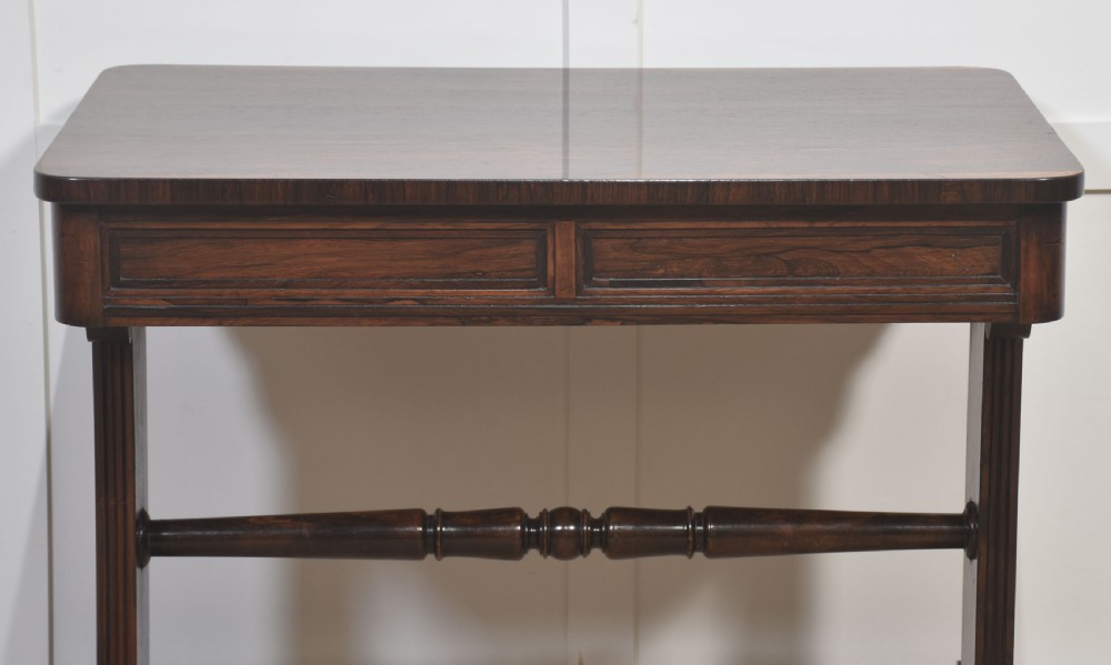 An antique Regency rosewood side table with turned stretcher and brass castors set against a white panelled wall. View VIII