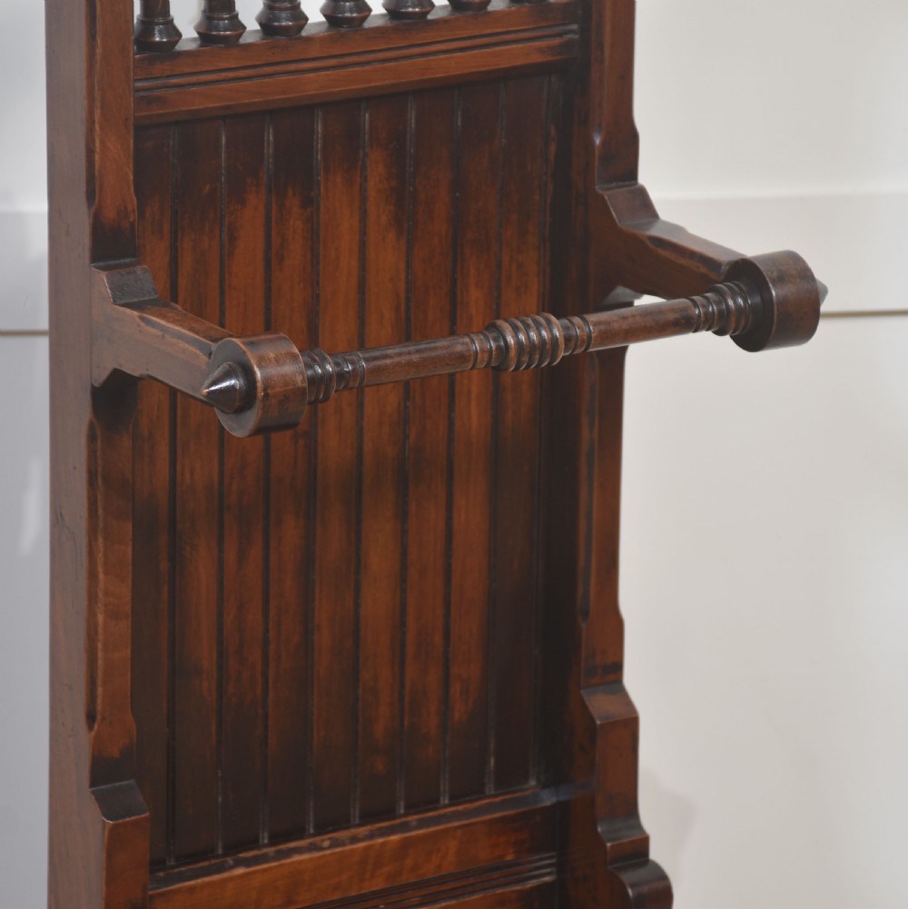 A tall dark wood Gothic Revival umbrella stand featuring a turned spindle gallery, horizontal support bar, trefoil cut-outs, and a circular brass drip tray. View VII