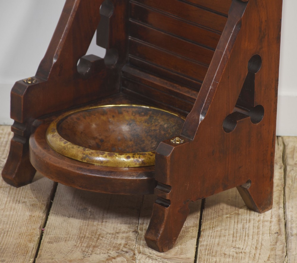 A tall dark wood Gothic Revival umbrella stand featuring a turned spindle gallery, horizontal support bar, trefoil cut-outs, and a circular brass drip tray. View IX