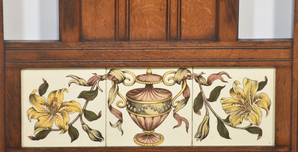 An antique oak umbrella stand featuring an arched top pediment, brass retaining rail, decorative ceramic floral tiles, and a lower drip tray. View VI