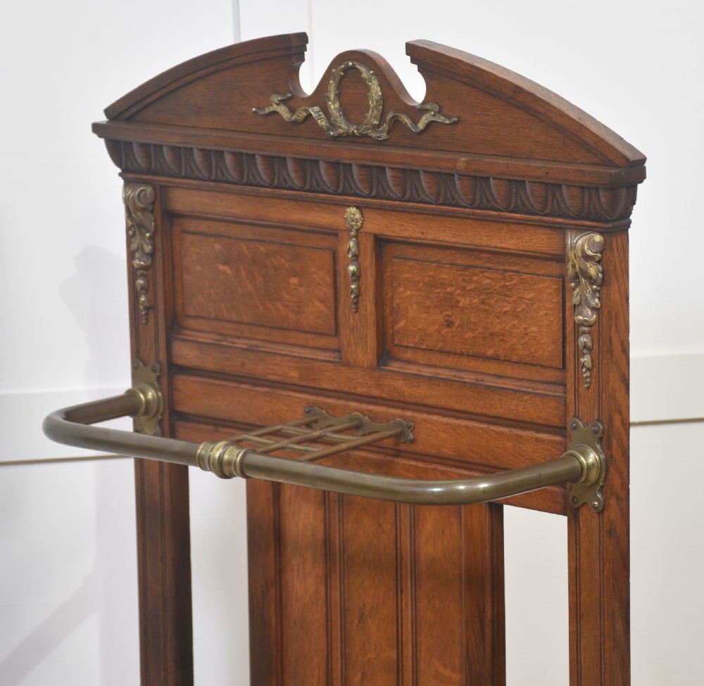 An antique oak umbrella stand featuring an arched top pediment, brass retaining rail, decorative ceramic floral tiles, and a lower drip tray. View XII