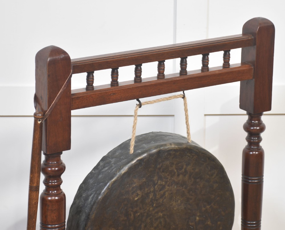 A freestanding dark mahogany frame with turned wooden pillars supporting a central circular brass gong disc and a suspended padded striker. View V