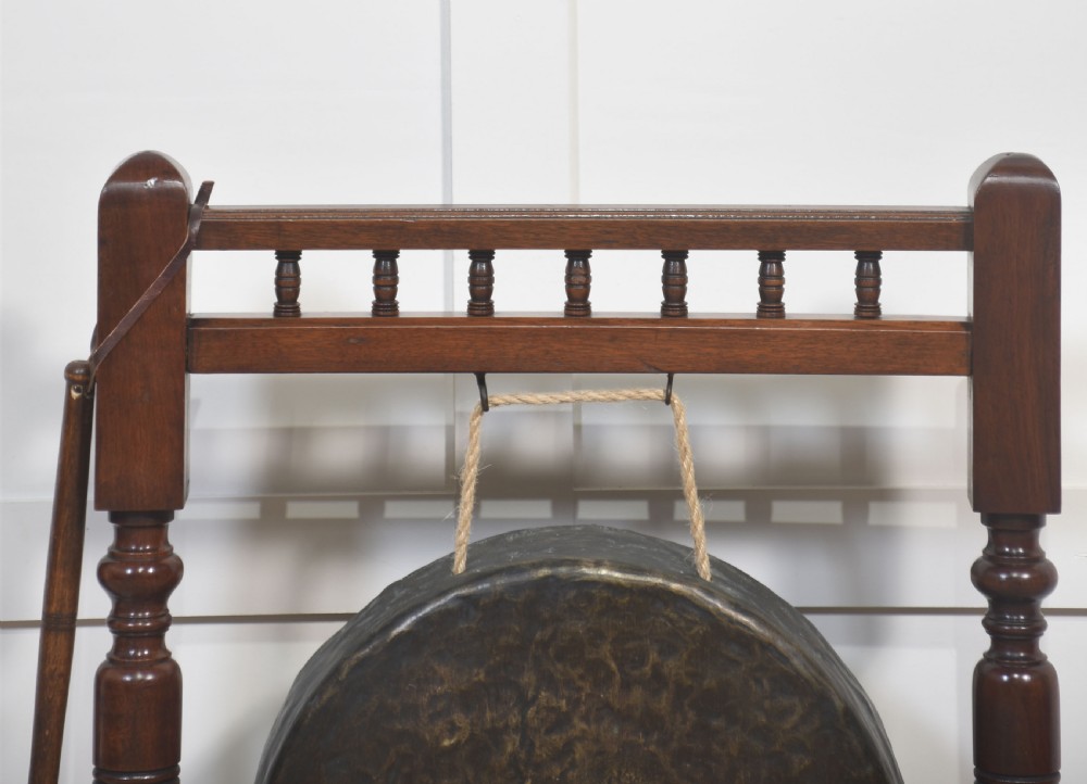 A freestanding dark mahogany frame with turned wooden pillars supporting a central circular brass gong disc and a suspended padded striker. View VI