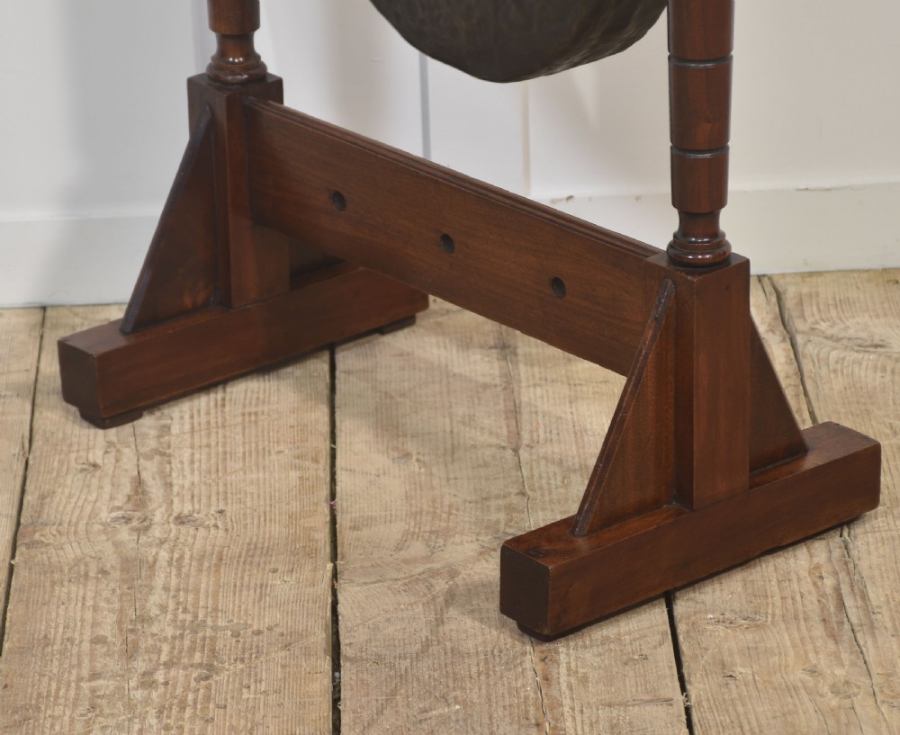 A freestanding dark mahogany frame with turned wooden pillars supporting a central circular brass gong disc and a suspended padded striker. View IX