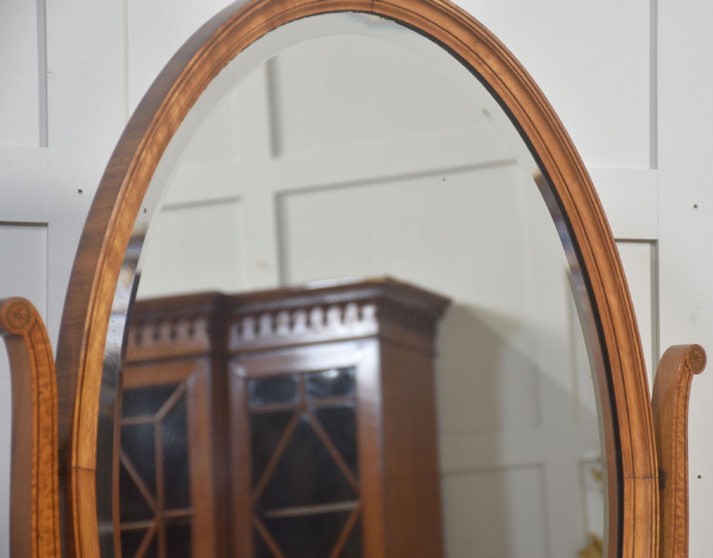 An oval satinwood dressing table mirror featuring marquetry inlay, curved supporting arms, and a two-drawer base resting on short turned feet. View X