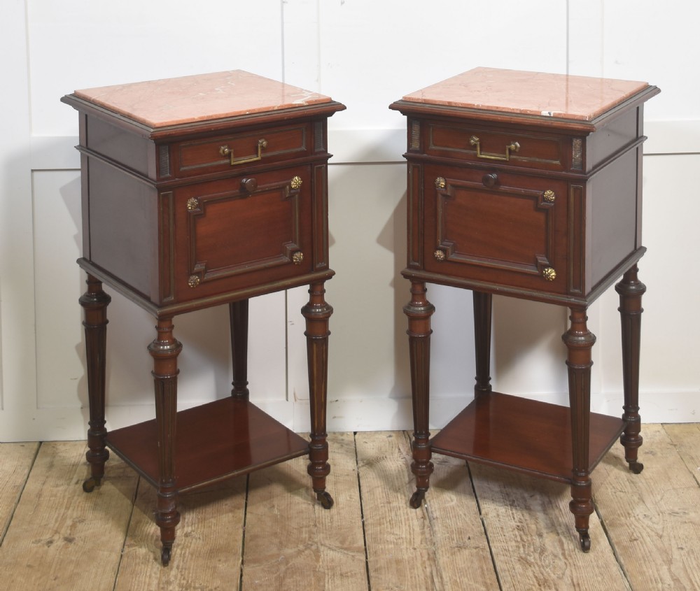 A matching pair of antique mahogany bedside cabinets with pink marble tops, single drawers, framed cupboard doors, lower shelves, and fluted legs on castors. View VI