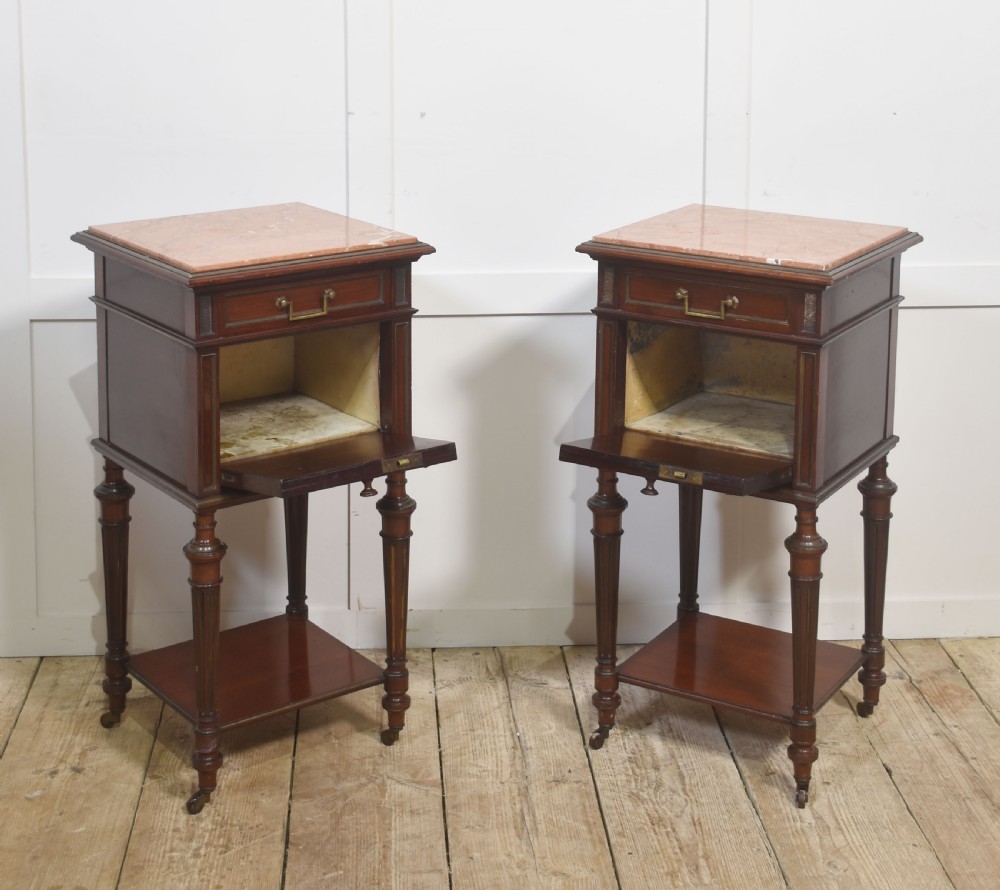 A matching pair of antique mahogany bedside cabinets with pink marble tops, single drawers, framed cupboard doors, lower shelves, and fluted legs on castors. View VII