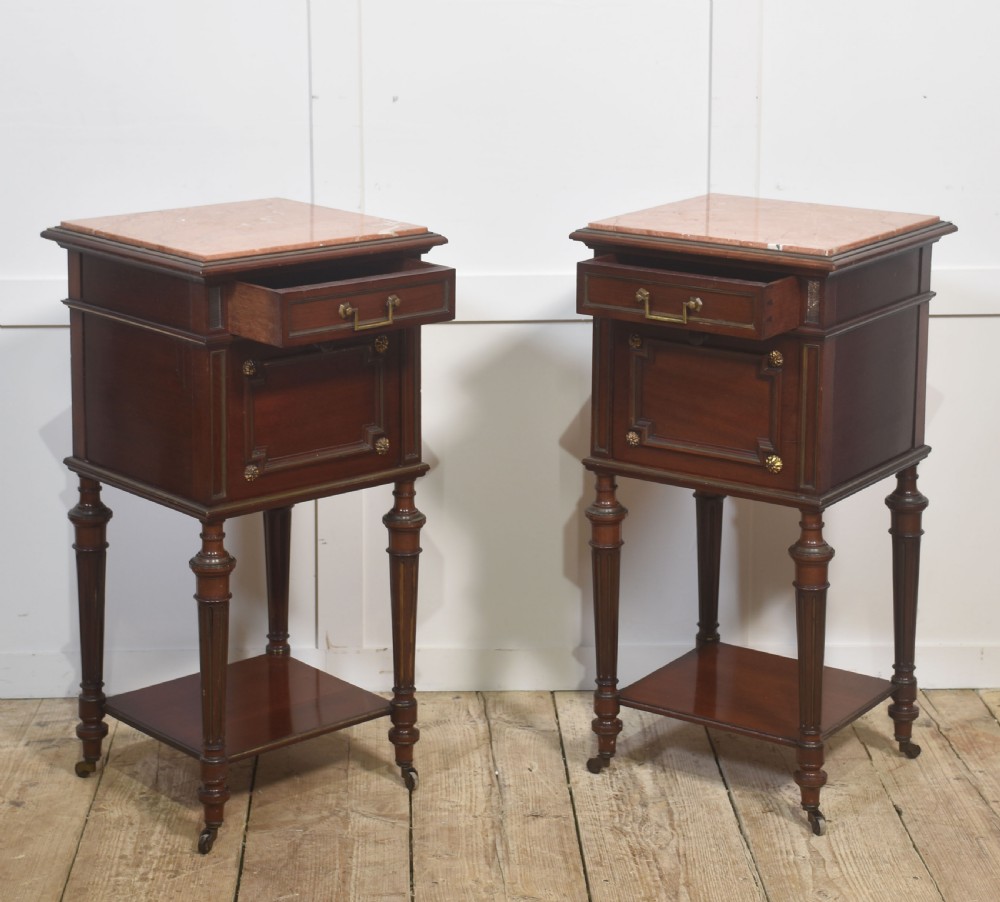 A matching pair of antique mahogany bedside cabinets with pink marble tops, single drawers, framed cupboard doors, lower shelves, and fluted legs on castors. View X