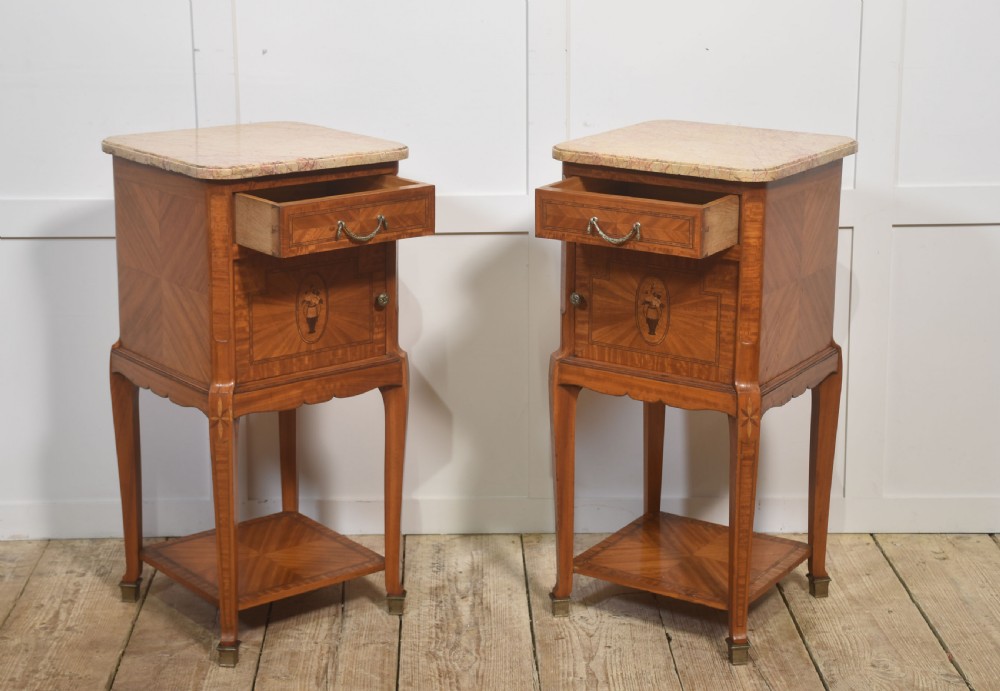 A pair of tall French satinwood bedside cabinets with marble tops, marquetry oval medallions, drawers, and slender legs. View X