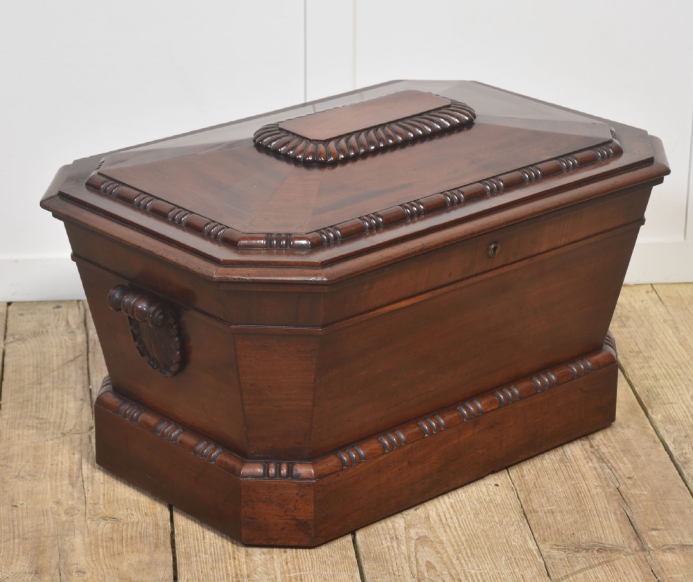 A Georgian dark mahogany sarcophagus-shaped cellarette featuring carved gadrooning around the lid and base, side handles, and a central keyhole.