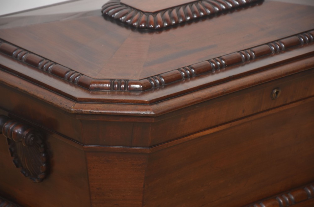 A Georgian dark mahogany sarcophagus-shaped cellarette featuring carved gadrooning around the lid and base, side handles, and a central keyhole. View II