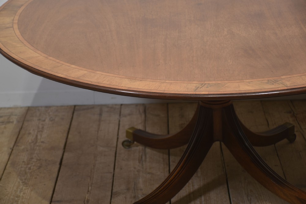 A circular Georgian-style mahogany dining table featuring a crossbanded inlay border, supported by a turned central pedestal with four reeded splayed legs on brass castors. View VIII