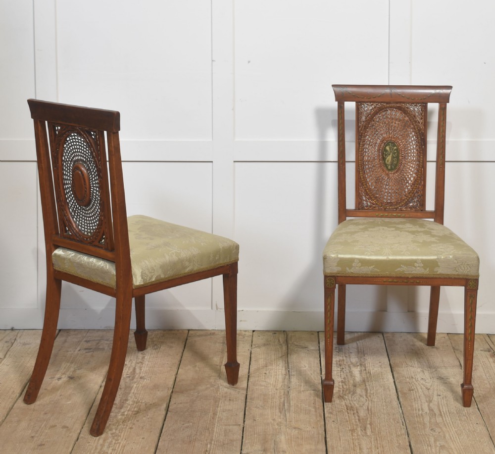 A pair of Edwardian satinwood side chairs featuring oval cane back panels with green painted central medallions, tapered legs, and pale green patterned silk seats. View II