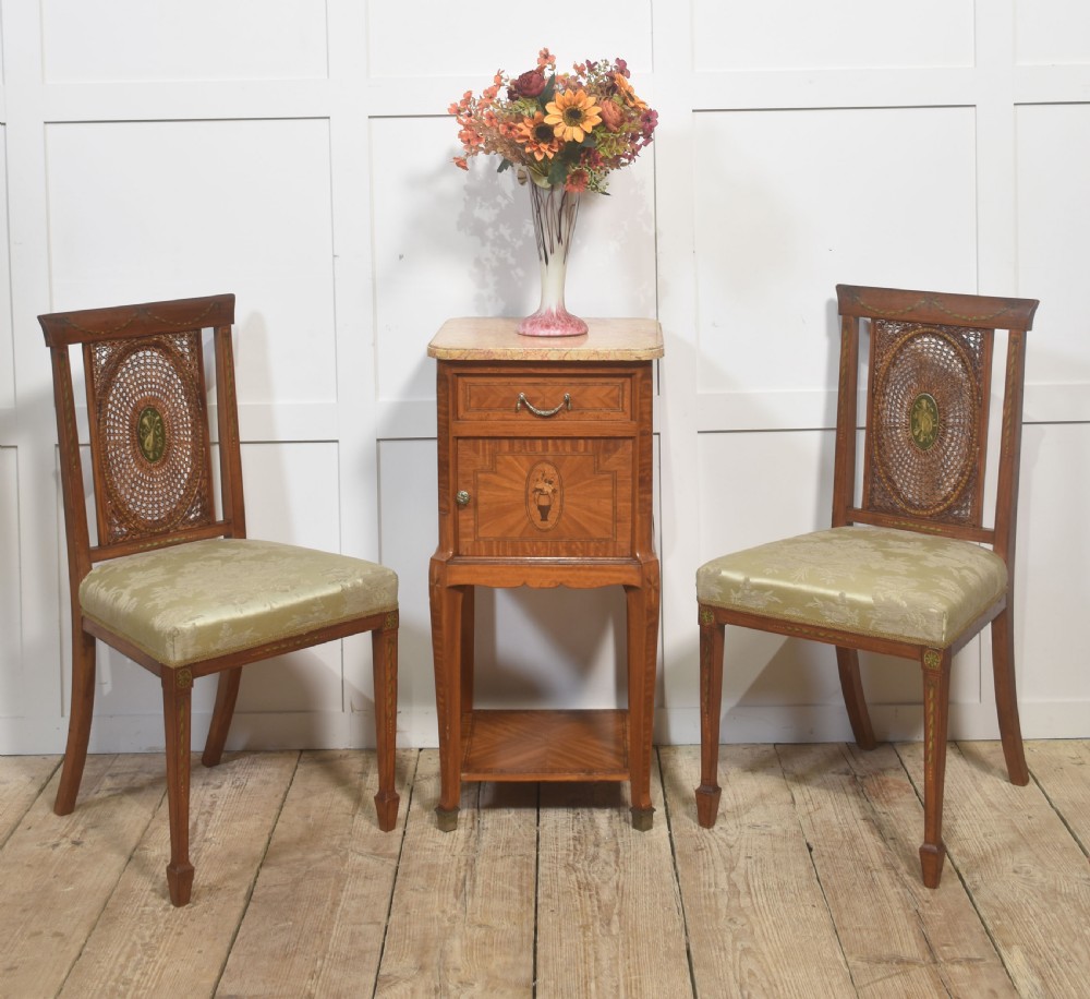 A pair of Edwardian satinwood side chairs featuring oval cane back panels with green painted central medallions, tapered legs, and pale green patterned silk seats. View V