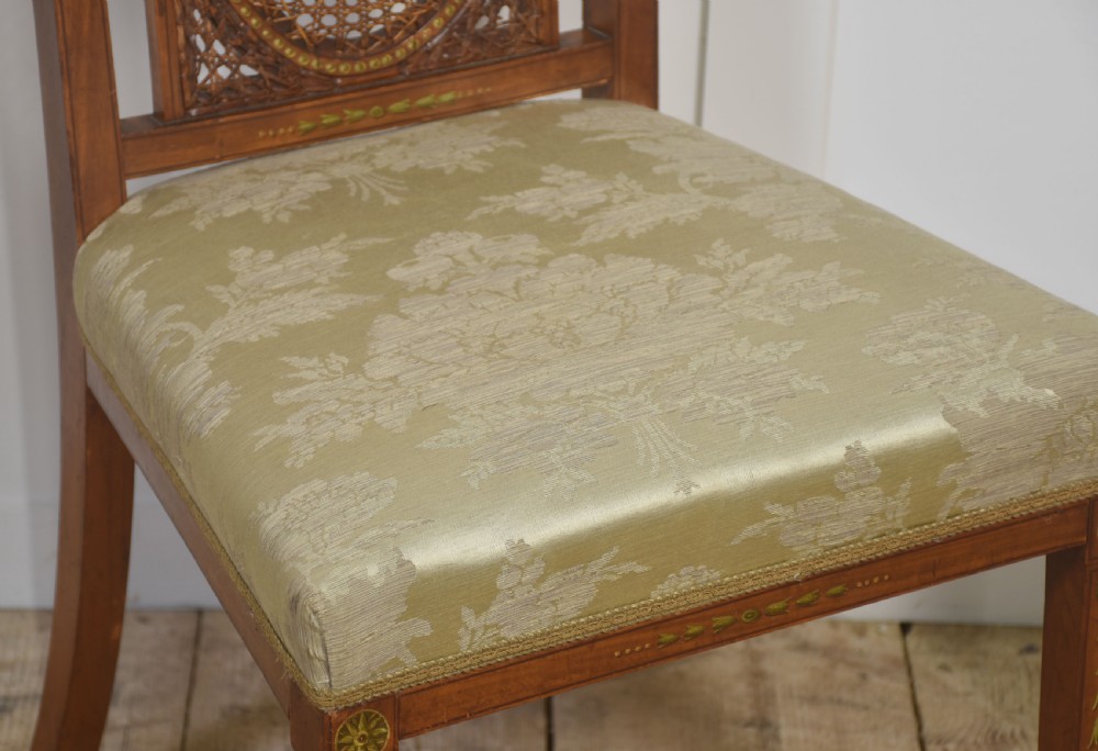 A pair of Edwardian satinwood side chairs featuring oval cane back panels with green painted central medallions, tapered legs, and pale green patterned silk seats. View VII