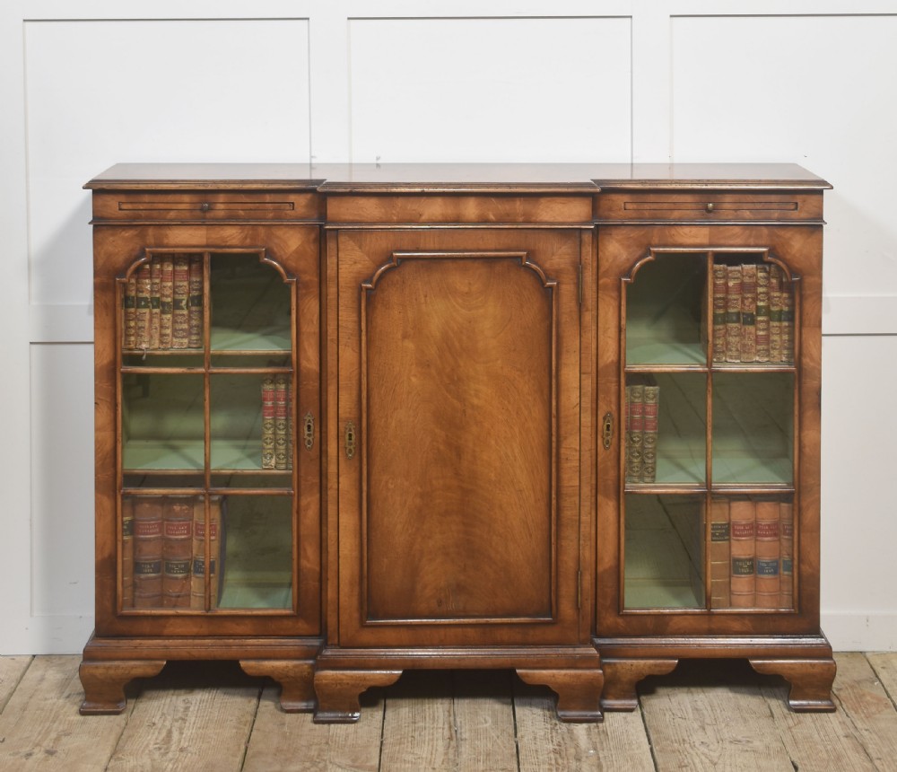 An early 20th-century walnut breakfront cabinet featuring a central solid wooden door flanked by two glazed doors, supported by bracket feet.