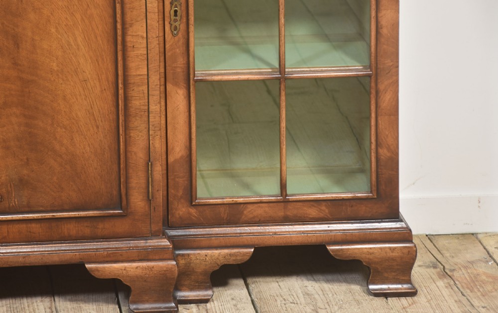 An early 20th-century walnut breakfront cabinet featuring a central solid wooden door flanked by two glazed doors, supported by bracket feet. View VII