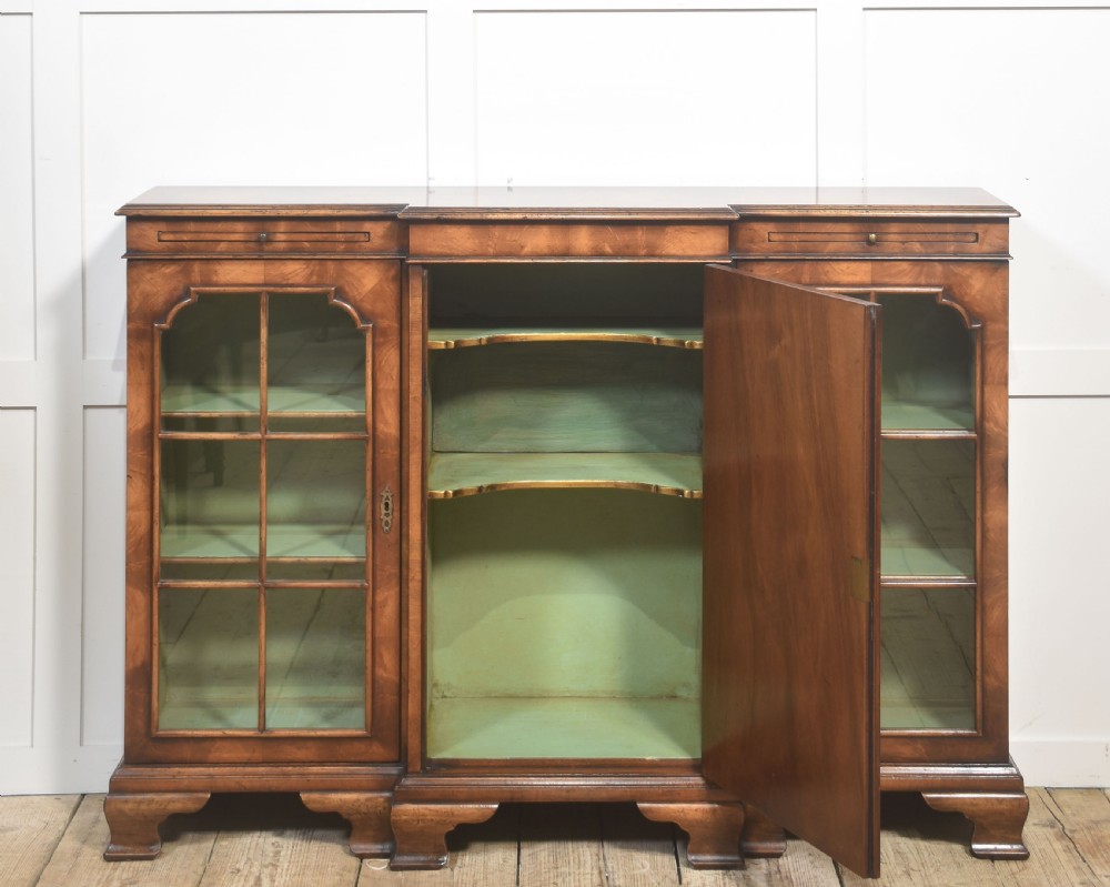 An early 20th-century walnut breakfront cabinet featuring a central solid wooden door flanked by two glazed doors, supported by bracket feet. View VIII