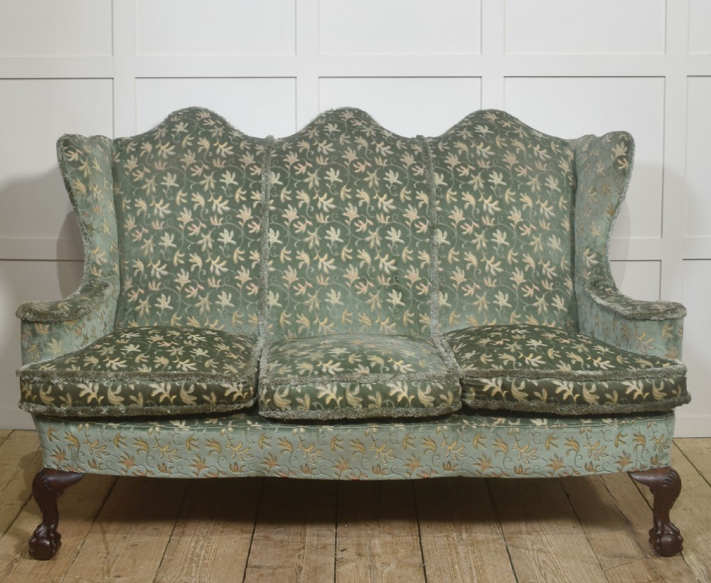 A Queen Anne style three-seat wingback sofa upholstered in patterned green fabric with carved cabriole legs and ball-and-claw feet.