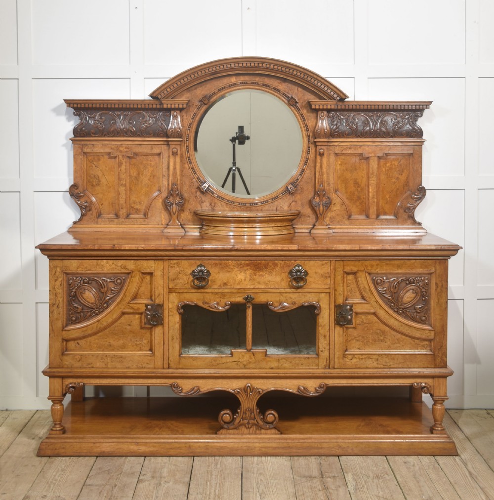 A Victorian carved pollard oak sideboard featuring an upper circular mirror back superstructure, drawers, glazed cabinet doors, and a lower pot board shelf.