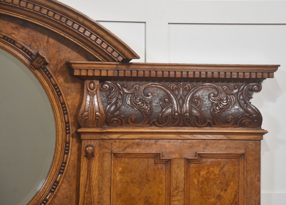 A Victorian carved pollard oak sideboard featuring an upper circular mirror back superstructure, drawers, glazed cabinet doors, and a lower pot board shelf. View III
