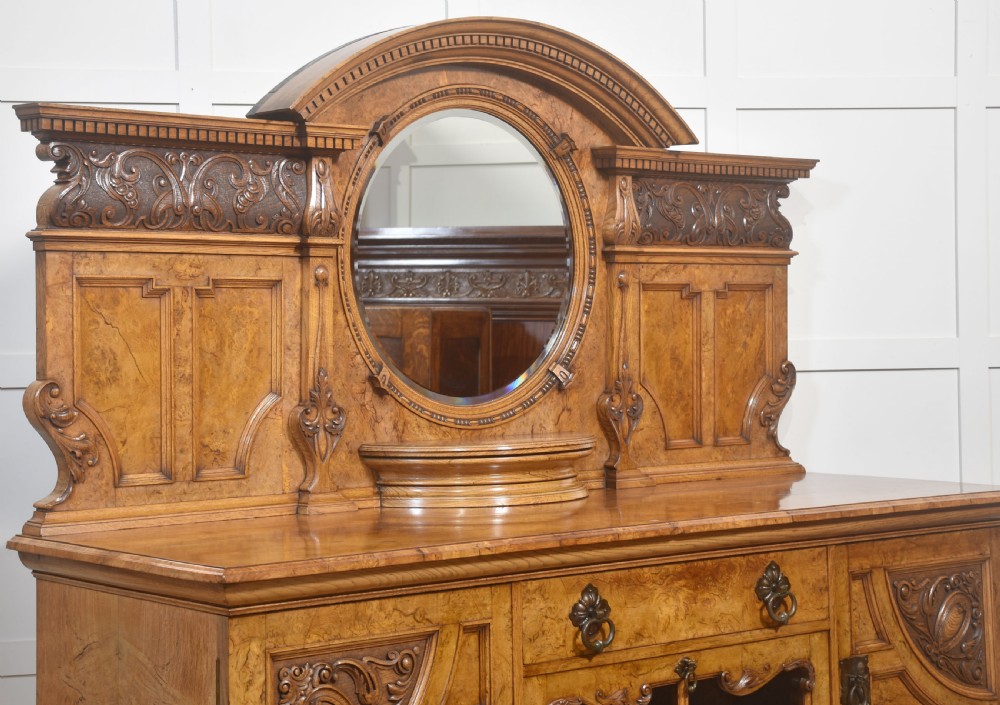 A Victorian carved pollard oak sideboard featuring an upper circular mirror back superstructure, drawers, glazed cabinet doors, and a lower pot board shelf. View XI