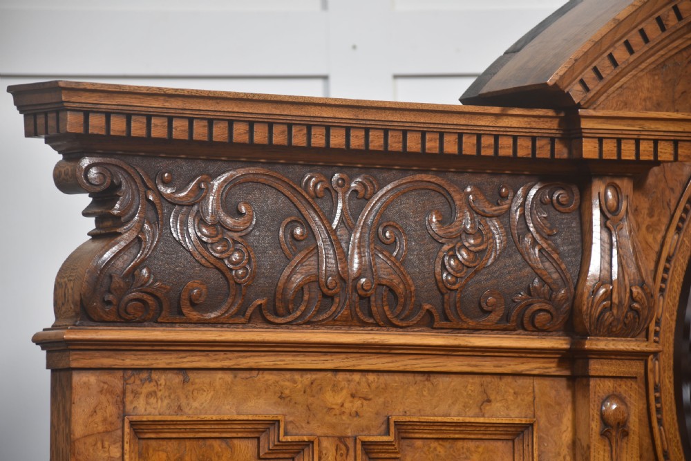 A Victorian carved pollard oak sideboard featuring an upper circular mirror back superstructure, drawers, glazed cabinet doors, and a lower pot board shelf. View XIII