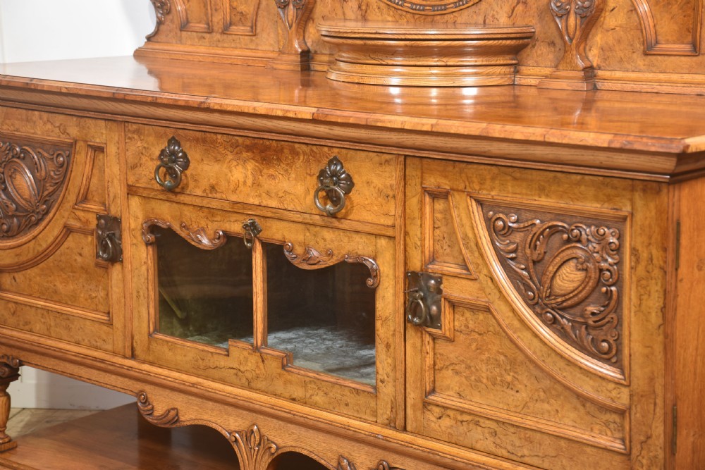 A Victorian carved pollard oak sideboard featuring an upper circular mirror back superstructure, drawers, glazed cabinet doors, and a lower pot board shelf. View XV