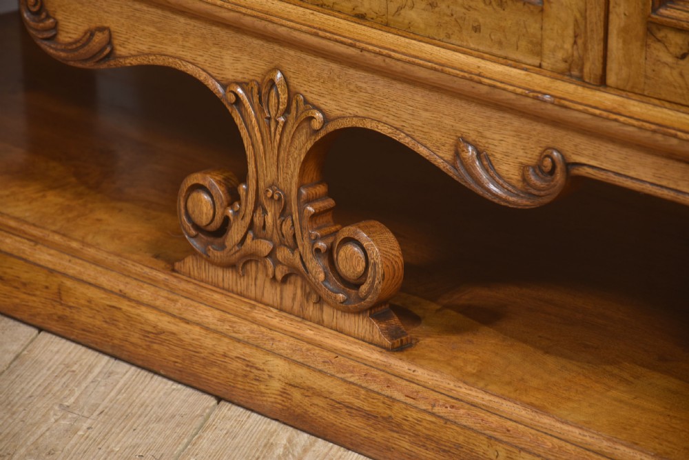 A Victorian carved pollard oak sideboard featuring an upper circular mirror back superstructure, drawers, glazed cabinet doors, and a lower pot board shelf. View XVI