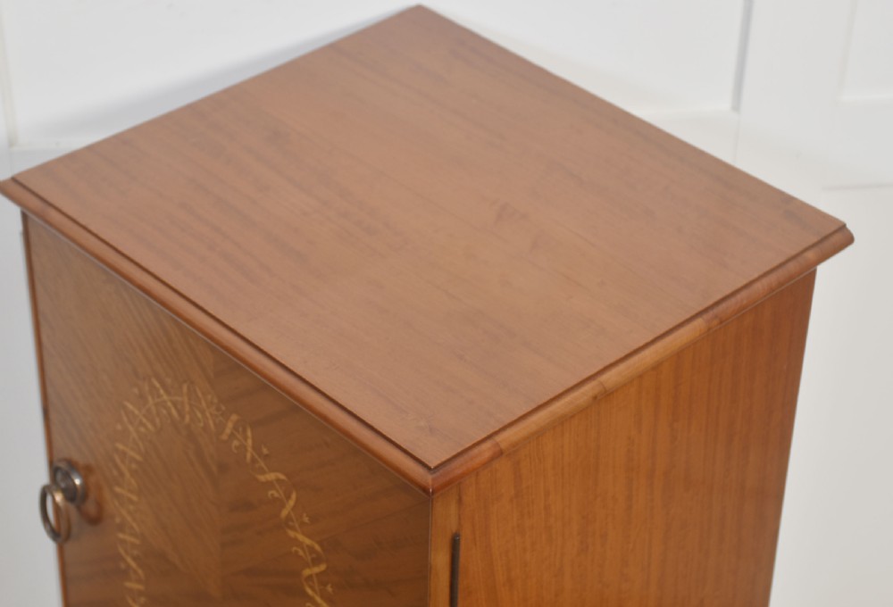 An Edwardian satinwood bedside cabinet featuring a chevron-veneered single door with an oval floral inlay and turned legs. View V