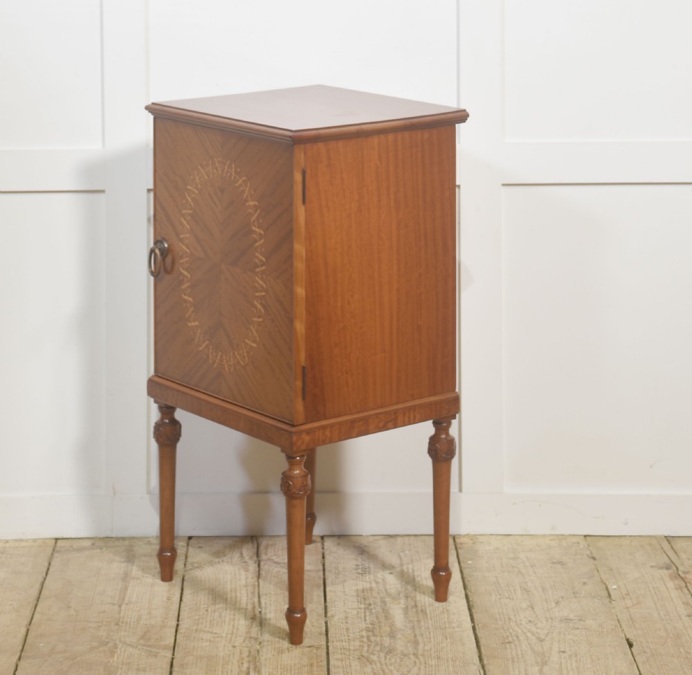 An Edwardian satinwood bedside cabinet featuring a chevron-veneered single door with an oval floral inlay and turned legs. View VI