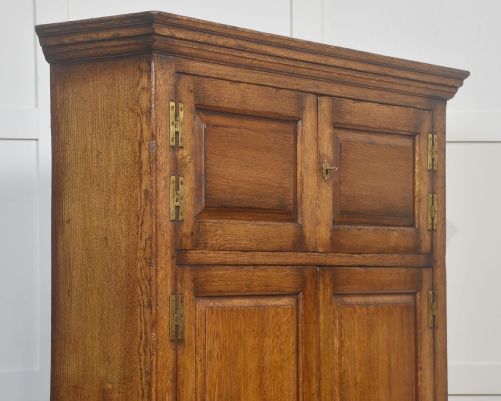 A tall solid oak hall seat cupboard featuring upper twin cupboard doors with exposed brass hinges, a flat wooden bench seat with turned arm supports, and lower drawers with brass drop handles. View IX