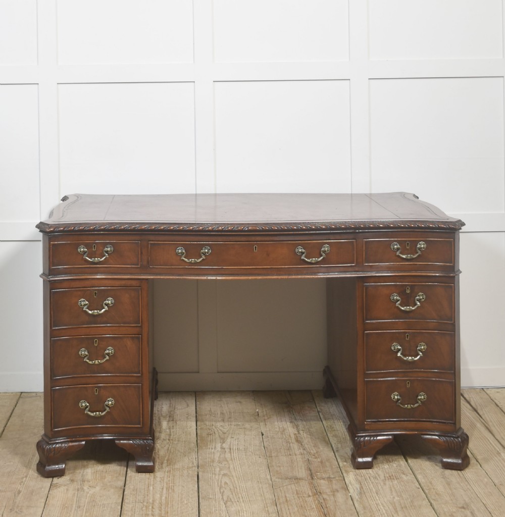 A polished mahogany twin-pedestal desk featuring brass swan-neck handles, carved edge moulding, and multiple drawers set on bracket feet.