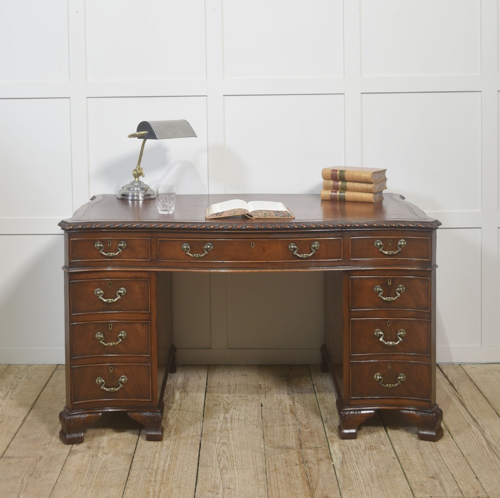 A polished mahogany twin-pedestal desk featuring brass swan-neck handles, carved edge moulding, and multiple drawers set on bracket feet. View III
