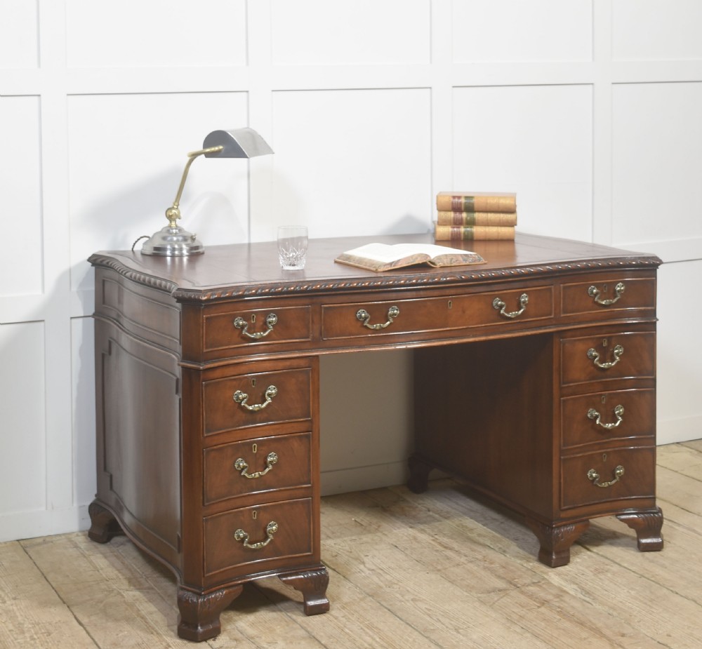 A polished mahogany twin-pedestal desk featuring brass swan-neck handles, carved edge moulding, and multiple drawers set on bracket feet. View IV