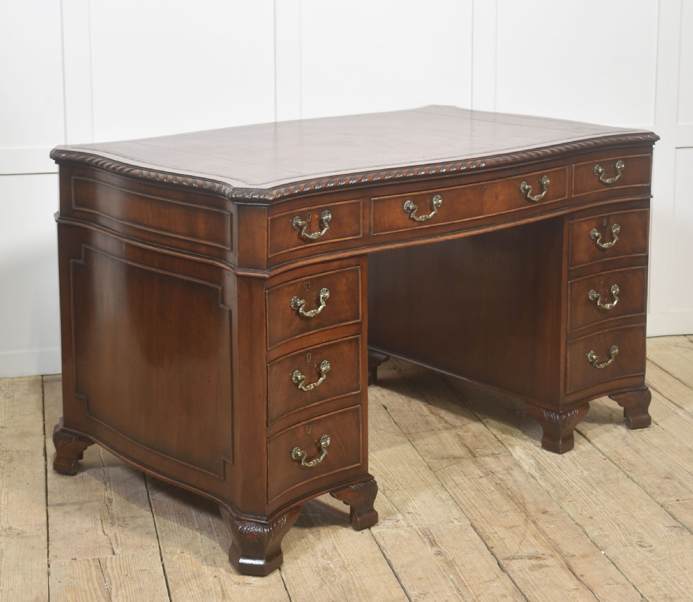 A polished mahogany twin-pedestal desk featuring brass swan-neck handles, carved edge moulding, and multiple drawers set on bracket feet. View V