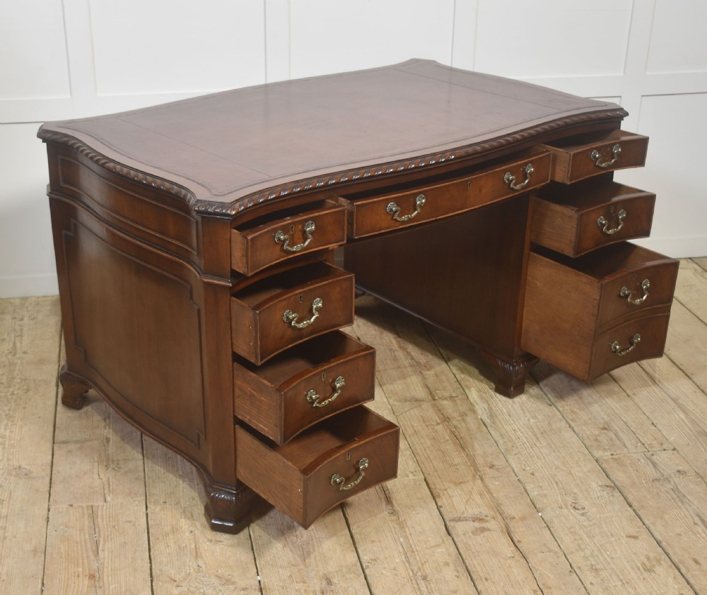 A polished mahogany twin-pedestal desk featuring brass swan-neck handles, carved edge moulding, and multiple drawers set on bracket feet. View VIII