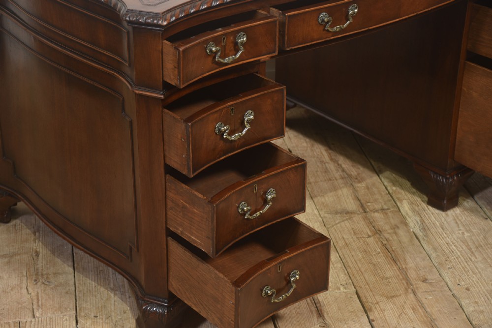 A polished mahogany twin-pedestal desk featuring brass swan-neck handles, carved edge moulding, and multiple drawers set on bracket feet. View IX