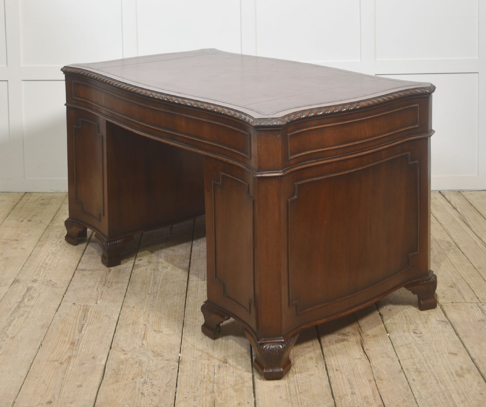 A polished mahogany twin-pedestal desk featuring brass swan-neck handles, carved edge moulding, and multiple drawers set on bracket feet. View XI