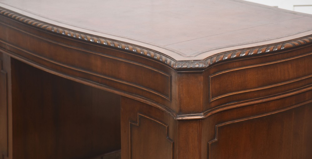 A polished mahogany twin-pedestal desk featuring brass swan-neck handles, carved edge moulding, and multiple drawers set on bracket feet. View XII