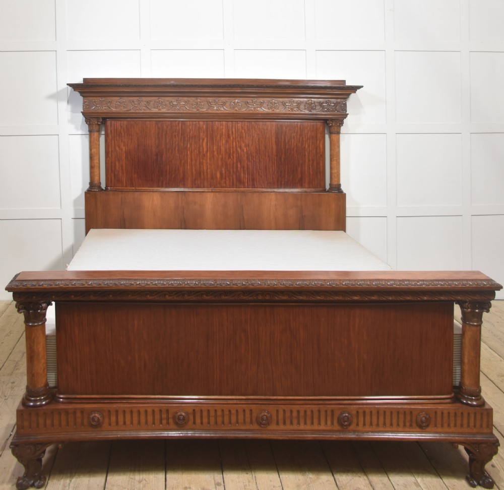 A carved mahogany super king size bed frame featuring architectural columns, a high headboard with flame mahogany panel, and carved decorative details.