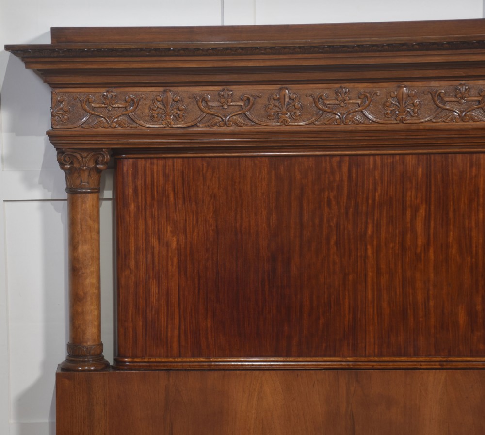 A carved mahogany super king size bed frame featuring architectural columns, a high headboard with flame mahogany panel, and carved decorative details. View V