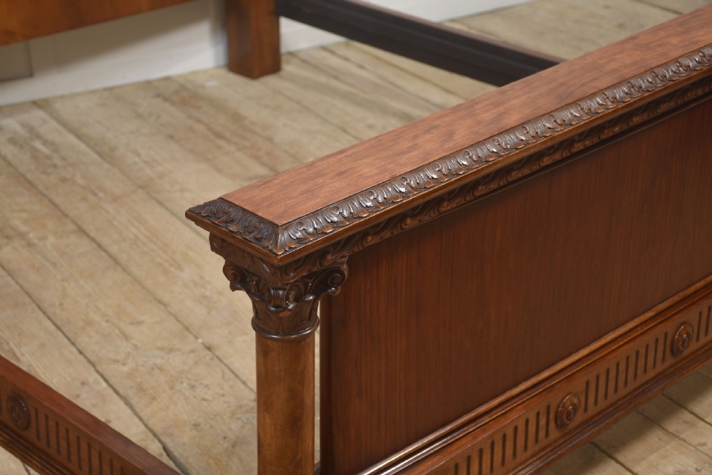 A carved mahogany super king size bed frame featuring architectural columns, a high headboard with flame mahogany panel, and carved decorative details. View X