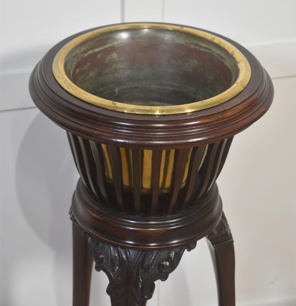 A dark mahogany wine cooler stand featuring a slatted circular bucket top with a fitted brass liner, supported by three carved legs connected by a central stretcher. View VI